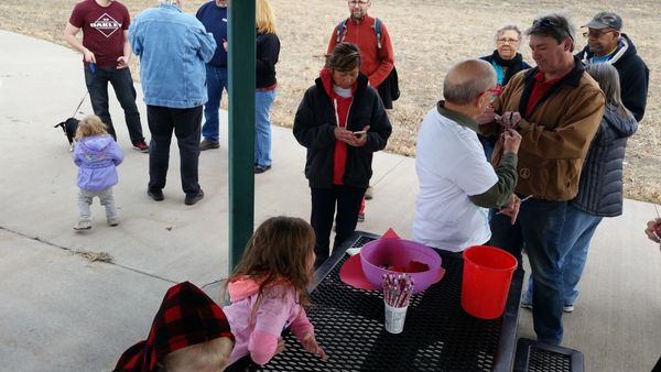 People gathered outdoors, some interacting near a picnic table with supplies.