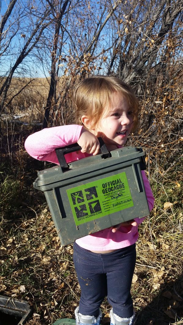 Child holding an official geocache container outdoors.