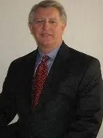 Man in a dark suit and red patterned tie posing against a plain background.