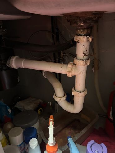 White PVC pipes and cleaning supplies under a sink.