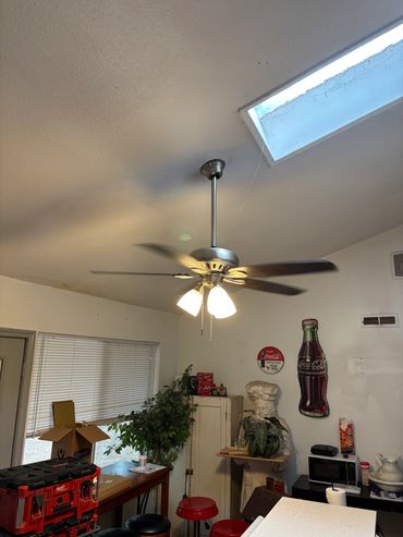 Ceiling fan spinning in a cluttered room with vintage Coca-Cola decor and plants.