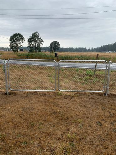 A metal chain-link gate with dry grass and a rural road in the background.