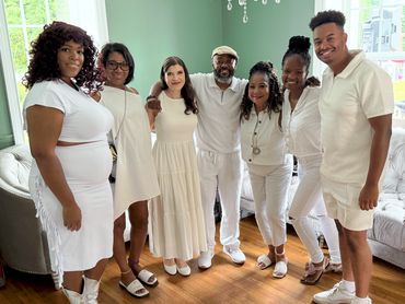 The Groovy Neighbors meet some new neighbors. A group of seven people dressed in white, smiling indoors.