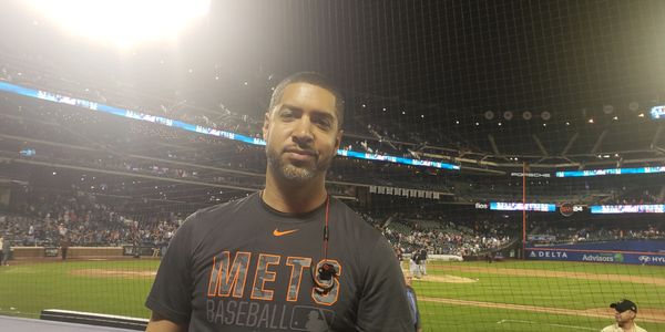 Christian Santamaria may be seen here at a NY Mets game in Citifield, at the first row seats directly behind the Mets dugout.