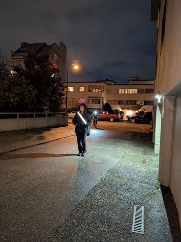 Pedestrian walking down the alley at night with illuminated strap. Cyclist behind with lights on.