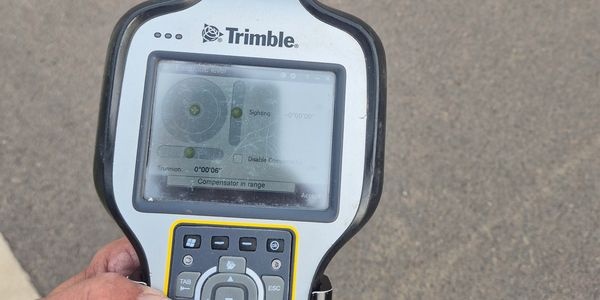 Handheld Trimble surveying device with screen displaying measurement data.