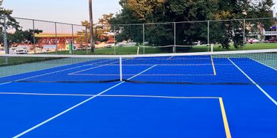 A vibrant blue pickleball court with a net in an outdoor park setting.