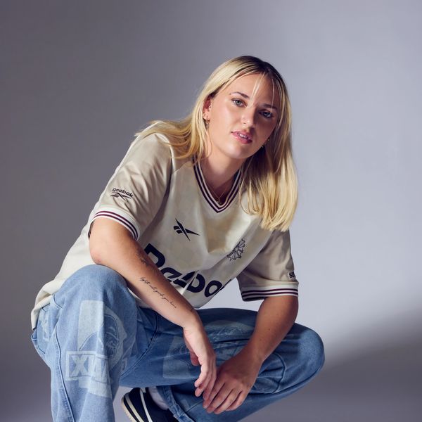 Young woman squatting in casual streetwear with a neutral background.