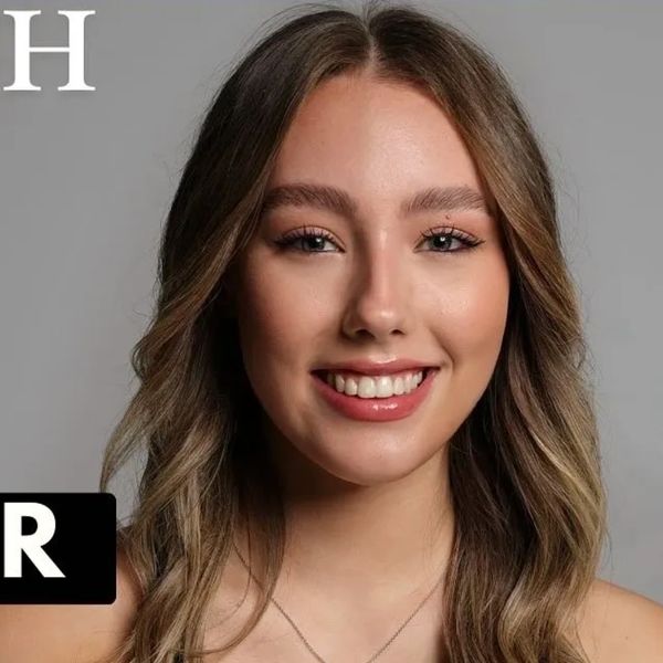 Close-up of a smiling young woman with wavy hair against a gray background.