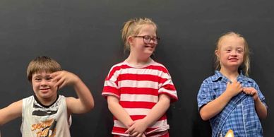 Three children with Down syndrome posing happily against a black background.