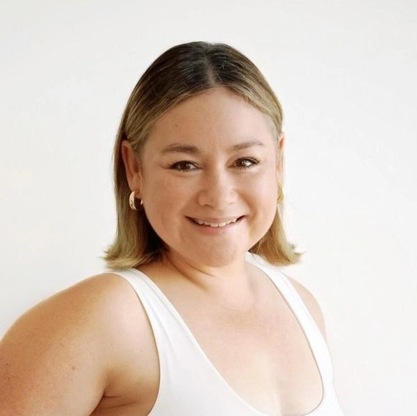 Smiling woman with short hair in a white sleeveless top against a plain background.