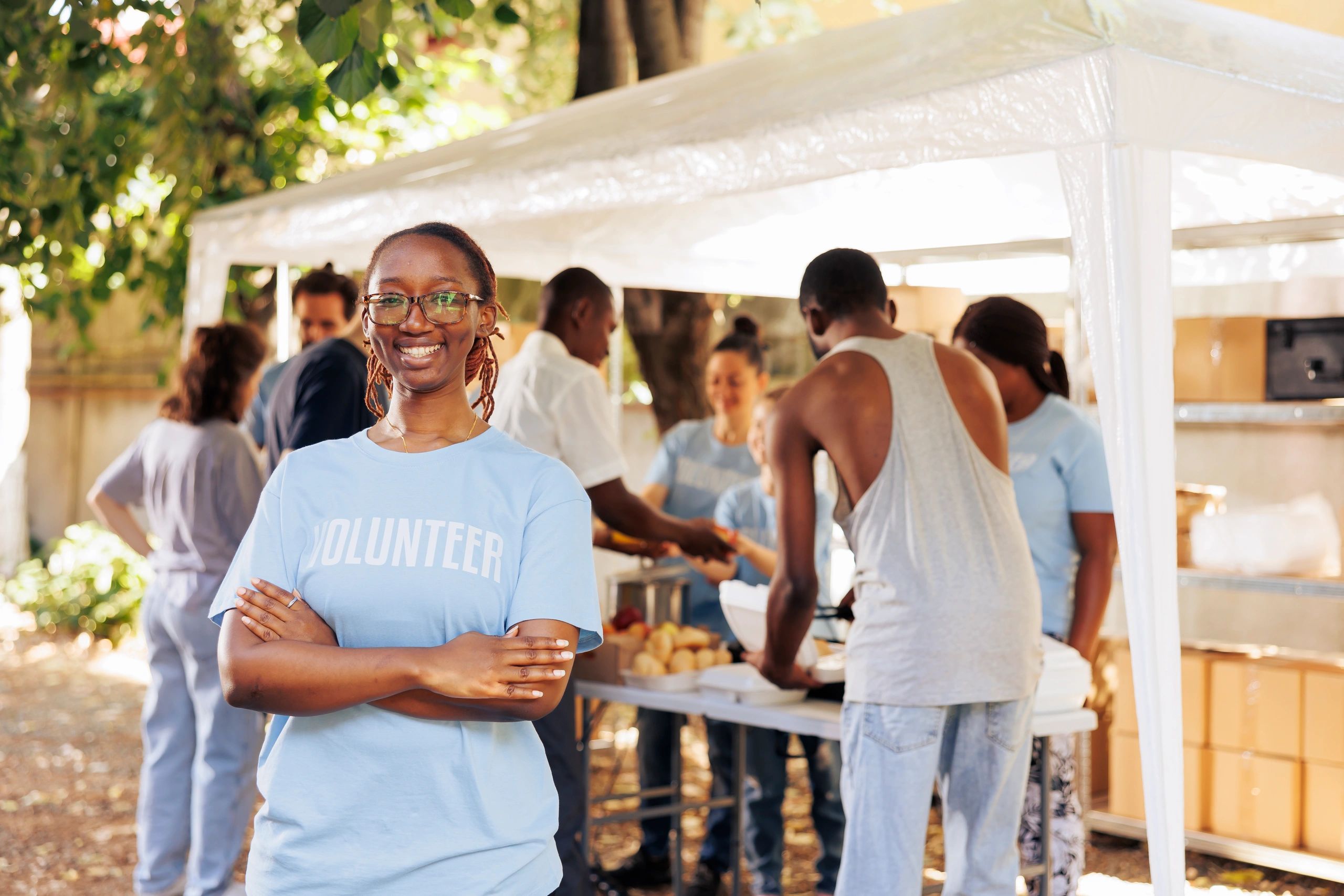 Smiling volunteer in front of a group serving food outdoors.