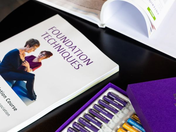 A foundation techniques book beside a colorful vitamin capsule set in a purple box.