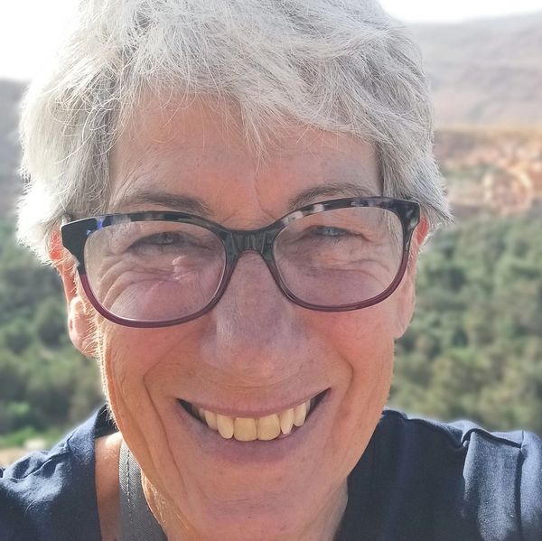 Smiling elderly woman with gray hair and glasses outdoors.