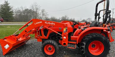 Orange Kubota tractor with front loader on gravel.