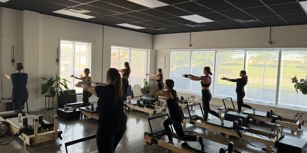 Group Pilates class practicing on reformer machines in a bright studio.