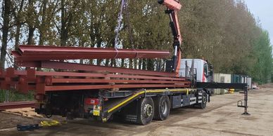 Truck unloading steel beams with crane.