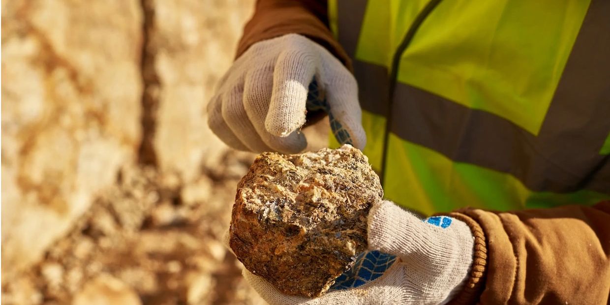 Worker in gloves holding a rock sample at a mining site.