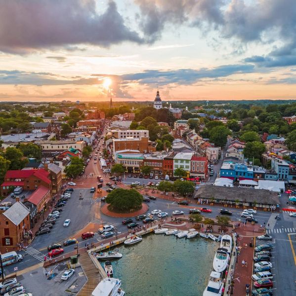 Sunset over a bustling harbor town with boats and historic buildings.