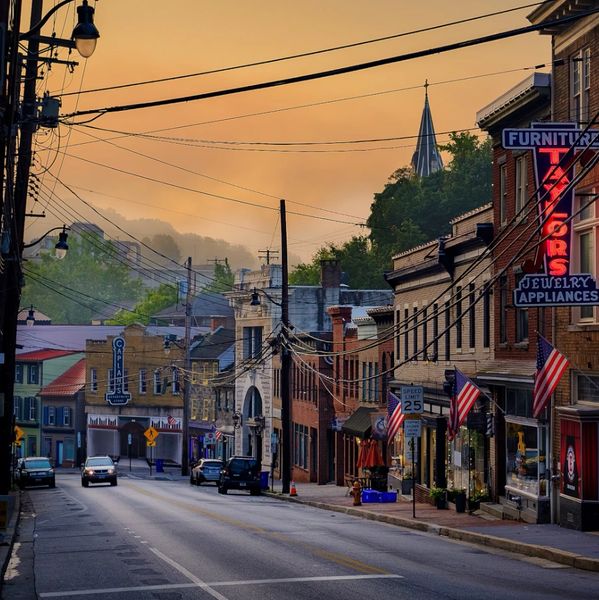 Quiet small-town street at sunset with shops and American flags.