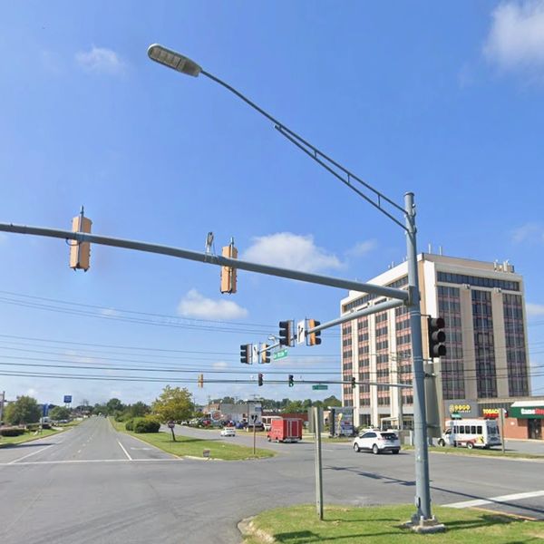 Intersection at 6th Avenue with traffic lights and a tall building under a clear blue sky.