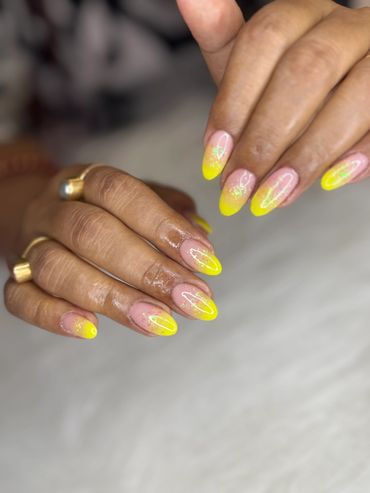 Hands with yellow ombre nails and subtle glitter accents.
