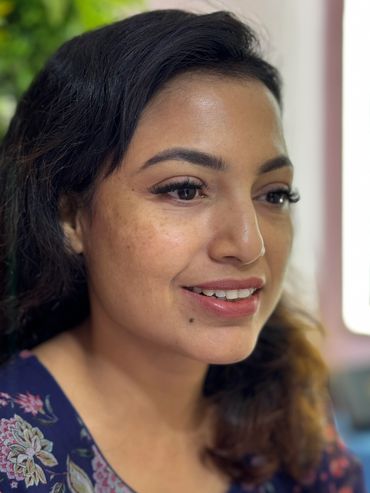 Close-up of a smiling woman with natural makeup and floral dress.