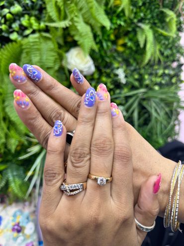 Colorful nail art on manicured hands with rings and bracelets.