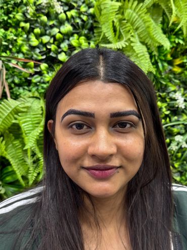 Smiling woman with long black hair and greenery background.