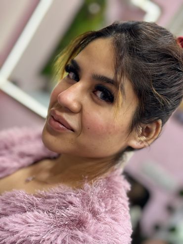 Close-up of a smiling woman with long eyelashes and fluffy pink attire.