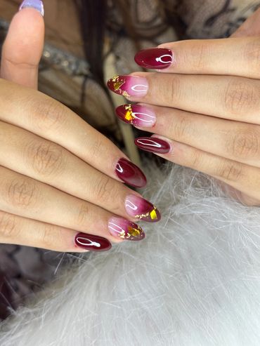 Elegant maroon gradient nails with gold foil accents on almond-shaped tips.