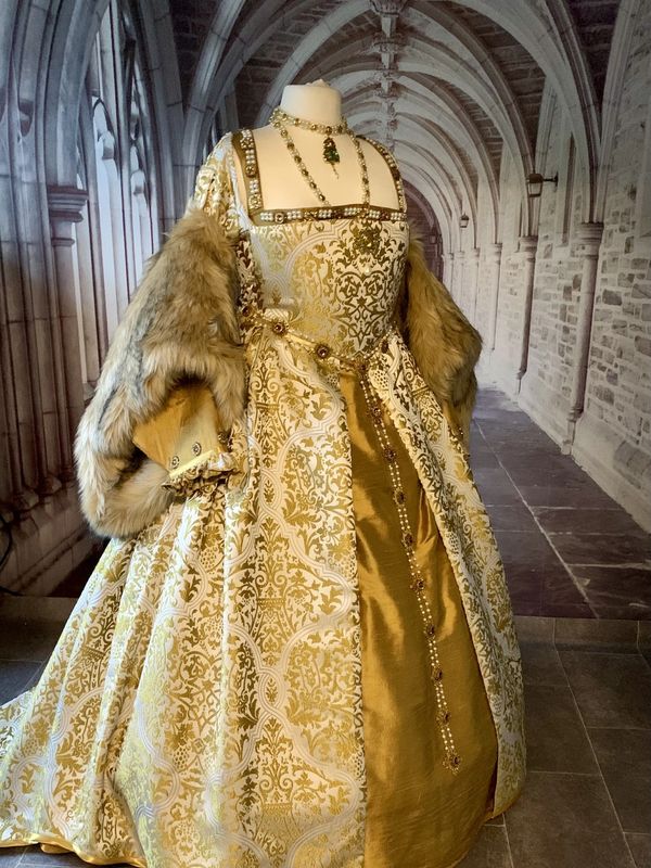 Ornate Renaissance gown with gold brocade and fur sleeves on a mannequin.