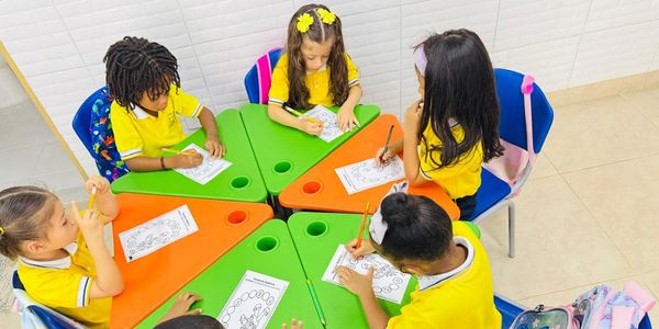 Niños coloreando en grupo en una mesa verde y naranja.