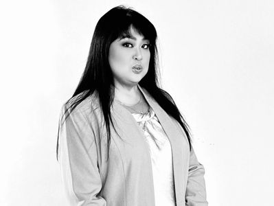 Woman with long dark hair wearing a blazer looks confidently at the camera.