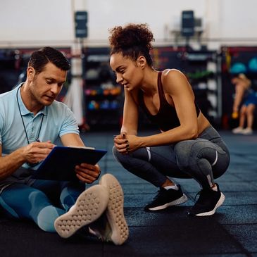 A fitness coach discusses a workout plan with a female athlete in a gym.