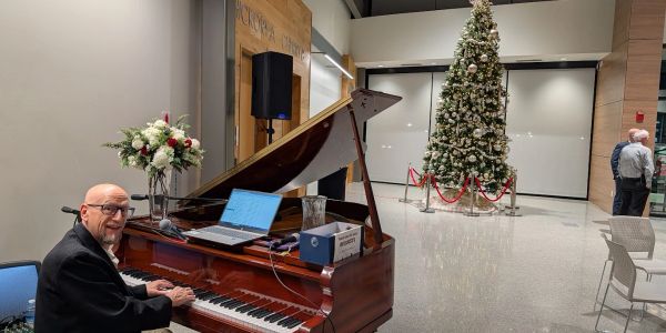 Man playing piano with Christmas tree in background.