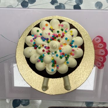 Chocolate cake topped with white frosting and colorful sprinkles on a gold base.