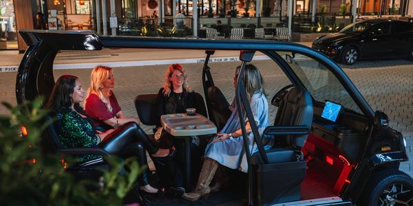 Four women sitting inside a small electric vehicle at night.
