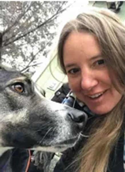 smiling woman with long blond hair shares camera spotlight with a black and white dog