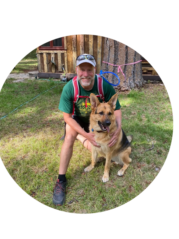 smiling man with a beard wears a baseball hat and athletic attire, hugs german shepherd dog