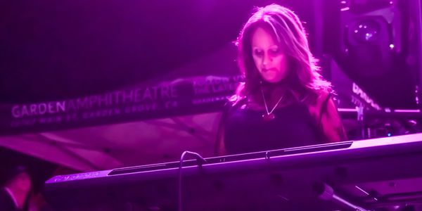 Woman playing keyboard on stage under purple lighting.