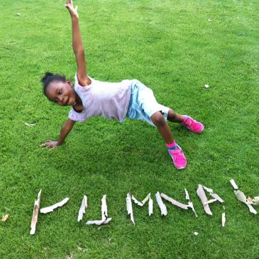 Girl posing on grass with word 'PUMNA!' spelled in sticks.