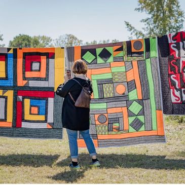 Person viewing colorful geometric quilts outdoors.