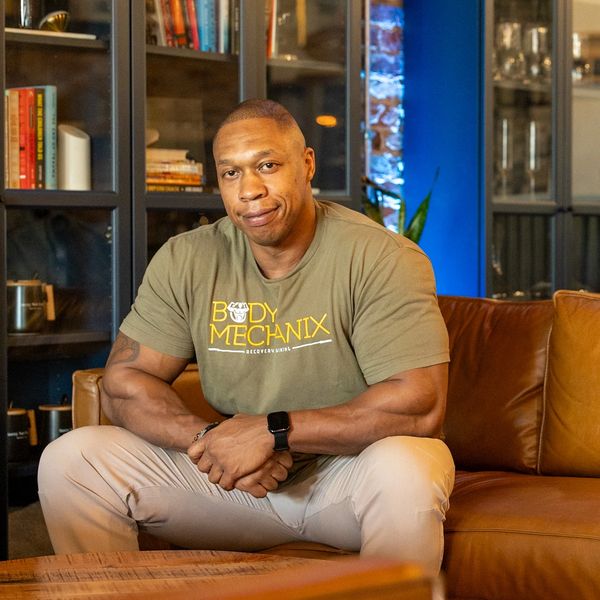 Muscular man sitting on a brown leather couch in a cozy room.