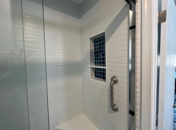 Shower with white porcelain tiles in a wave pattern and a blue-tiled caddy inset