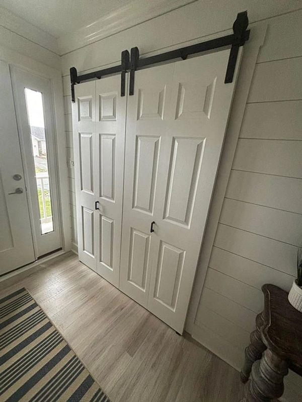 Entry hall with barn doors and soft white shiplap walls gives an open airy feeling to a narrow space