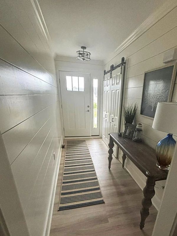 Entry hall with barn doors and soft white shiplap walls gives an open airy feeling to a narrow space