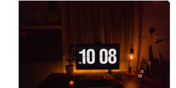 Dark workspace illuminated by a clock on a screen and a lamp.