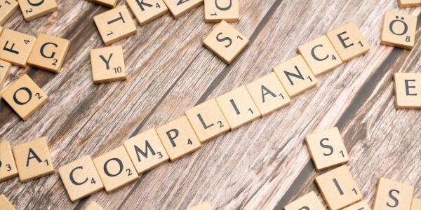 Scrabble tiles spelling "COMPLIANCE" on a wooden surface.
