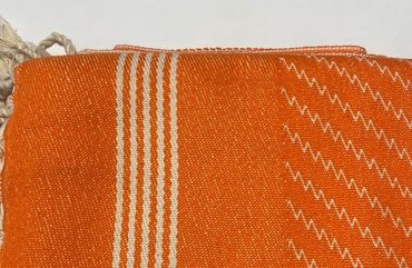 Folded orange and white woven textile with fringes on one side.